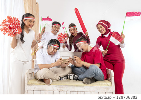 Portrait of an Indonesian southeast asian people celebrating Indonesia Independence Day on the 17th of August with a game of playing video games on cellphone at home. Concept of Kemerdekaan Indonesia Portrait of an Indonesian southeast asian people celebrating Indonesia Independence Day on the 17th of August with a game of playing video games on cellphone at home. Concept of Kemerdekaan Indonesia 128736882
