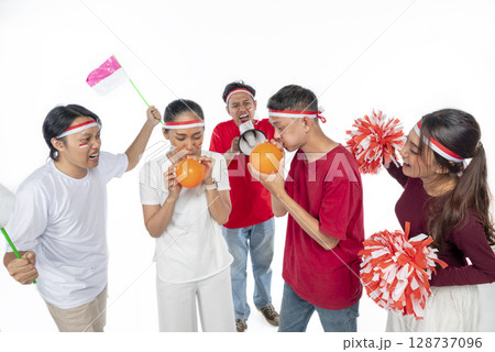 Portrait of an Indonesian southeast asian people celebrate Indonesia Independence Day on 17th of August with a game of blowing balloons isolated over white background. Concept of Kemerdekaan Indonesia Portrait of an Indonesian southeast asian people celebrate Indonesia Independence Day on 17th of August with a game of blowing balloons isolated over white background. Concept of Kemerdekaan Indonesia 128737096