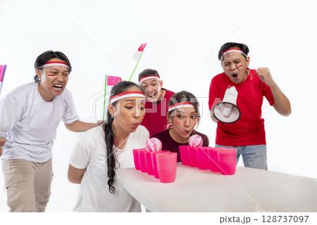 Portrait of an Indonesian southeast asian people celebrate Indonesia Independence Day 17th of August with game blowing ball on plastic glass isolated white background. Concept of Kemerdekaan Indonesia 128737097