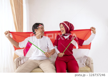 Portrait of an Indonesian southeast asian people celebrating Indonesia Independence Day on the 17th of August by holding the Indonesian national flag at home. Concept of Kemerdekaan Indonesia Portrait of an Indonesian southeast asian people celebrating Indonesia Independence Day on the 17th of August by holding the Indonesian national flag at home. Concept of Kemerdekaan Indonesia 128737246