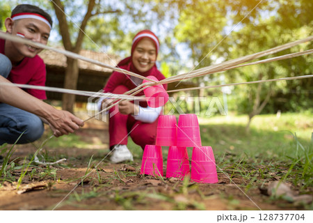 Portrait of an Indonesian southeast asian people celebrate Indonesia Independence Day on the 17th of August with a game of building a plastic glass stack with a stick outdoors. Concept of Kemerdekaan 128737704