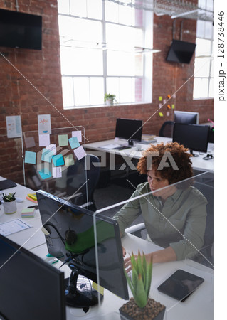 Man working on desktop computer and tablet at open-plan office desk with sticky notes, copy space Man working on desktop computer and tablet at open-plan office desk with sticky notes, copy space 128738446