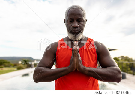 Mature African American man performing yoga outdoors near pool, channeling calm mindfulness 128738466