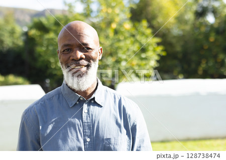 Senior African American man standing in garden, wearing light blue button-down shirt, smiling Senior African American man standing in garden, wearing light blue button-down shirt, smiling 128738474