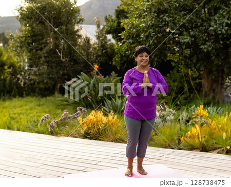 Senior mixed woman practicing yoga on pink yoga mat in outdoor garden, exuding calm energy 128738475