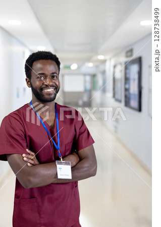 Young African American man standing in hospital corridor, wearing scrubs and blue lanyard ID badge 128738499