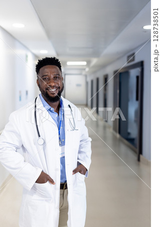 African American doctor standing in hospital corridor, wearing lab coat with stethoscope, ID badge 128738501