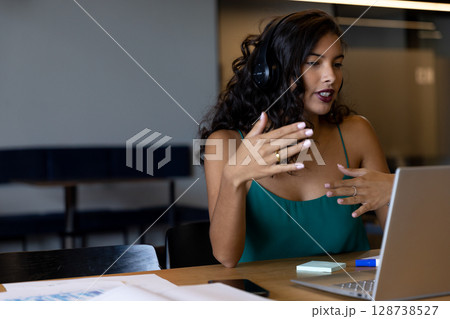 woman gesturing at laptop in modern coworking space, with headphones and sticky notes, copy space 128738527