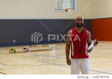 African American man coaching basketball in gym with clipboard, stopwatch and whistle, copy space African American man coaching basketball in gym with clipboard, stopwatch and whistle, copy space 128738556