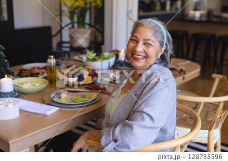 Senior woman enjoying meal at table indoors, smiling at camera with charcuterie board, copy space 128738596