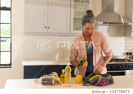 Sorting senior woman arranging vegetables at kitchen island, with mesh produce bags, copy space 128738671