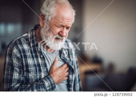 An elderly man holds his chest with his hand, expressing intense pain or discomfort, and his face and eyes show suffering and anxiety. 128739002