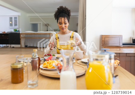 Woman enjoying breakfast at wooden table in kitchen, with glass pitchers of milk and orange juice Woman enjoying breakfast at wooden table in kitchen, with glass pitchers of milk and orange juice 128739014