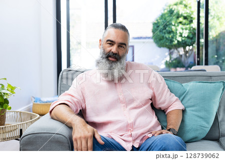Man sitting on gray sofa at home, with wicker table, potted plant and sliding glass door Man sitting on gray sofa at home, with wicker table, potted plant and sliding glass door 128739062