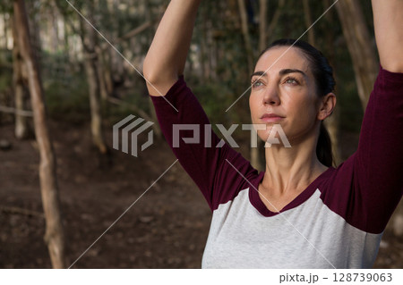 Woman stretching arms overhead in wooded forest clearing, with soft light filtering, copy space Woman stretching arms overhead in wooded forest clearing, with soft light filtering, copy space 128739063