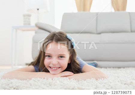 female child lying on stomach on white fluffy rug in living room with blue hair bow 128739073