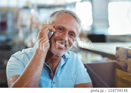Middle-aged man talking on smartphone in modern café interior, showcasing casual digital connection Middle-aged man talking on smartphone in modern café interior, showcasing casual digital connection 128739136