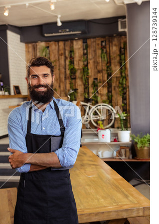 Young adult man wearing apron, working behind wooden counter in cozy café, with bicycle wall art Young adult man wearing apron, working behind wooden counter in cozy café, with bicycle wall art 128739144