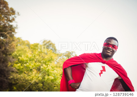 African American man posing in park near trees and sky, wearing red cape, mask, lightning t-shirt African American man posing in park near trees and sky, wearing red cape, mask, lightning t-shirt 128739146