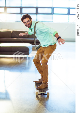 Young adult male riding skateboard in modern indoor lounge, with eyeglasses and crossbody satchel Young adult male riding skateboard in modern indoor lounge, with eyeglasses and crossbody satchel 128739149