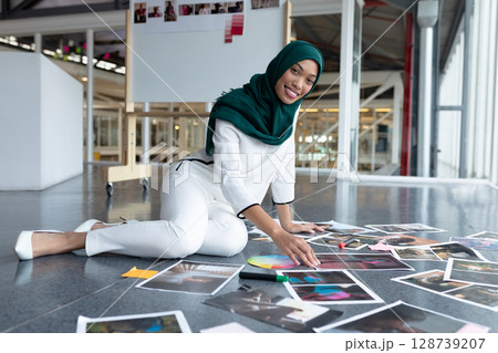 Woman wearing green hijab kneeling and arranging photographs and swatches on modern studio floor Woman wearing green hijab kneeling and arranging photographs and swatches on modern studio floor 128739207