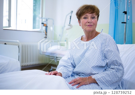 Senior woman sitting on hospital bed in hospital room, with IV pole, copy space 128739252