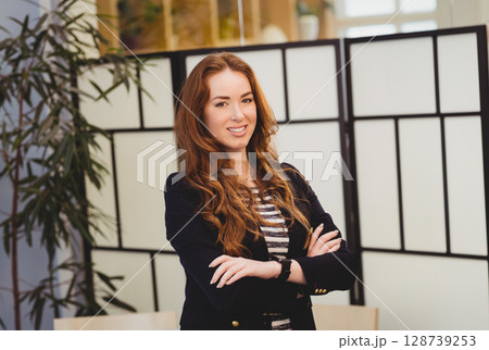 Woman standing confidently in office space, with smartwatch, glass divider and bamboo plant 128739253