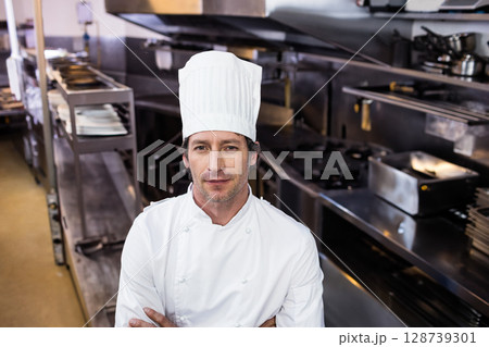 Male chef wearing coat and hat, working in commercial kitchen with steel ovens and stovetops Male chef wearing coat and hat, working in commercial kitchen with steel ovens and stovetops 128739301