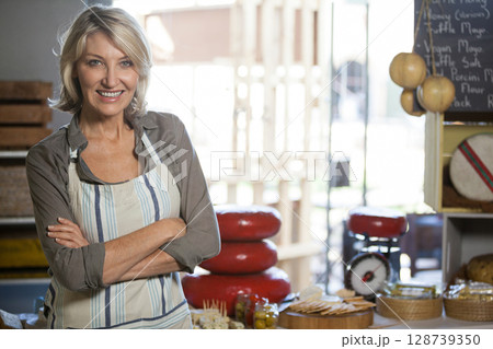 Woman standing behind counter in craft cheese shop, showcasing red-waxed wheels and vintage scale 128739350