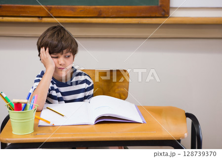 School-aged boy resting head on hand at desk in classroom, with open notebook, copy space School-aged boy resting head on hand at desk in classroom, with open notebook, copy space 128739370