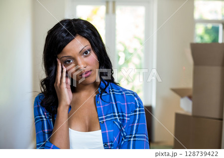 Resting head on hand, woman gazing at bright window in hallway, with stacked moving boxes 128739422