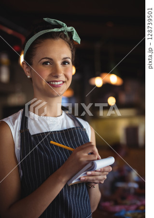 Smiling female server taking orders in cozy restaurant interior, with notepad and pencil 128739501