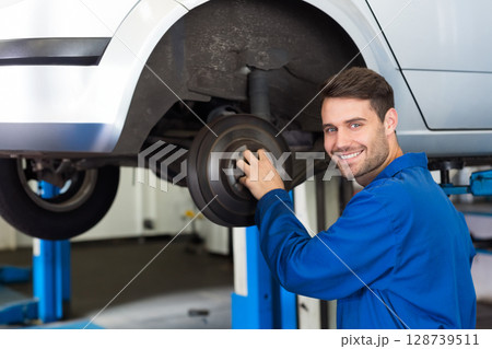 Mid-adult male mechanic inspecting brake drum on car inside garage, with lift pillars, copy space 128739511