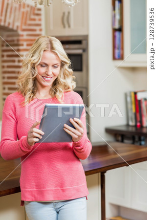 Leaning woman holding tablet and browsing recipes at home kitchen counter, showing cookbooks 128739536
