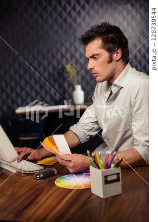 Holding fan of color swatches man working at office desk, with computer, color wheel, copy space Holding fan of color swatches man working at office desk, with computer, color wheel, copy space 128739544