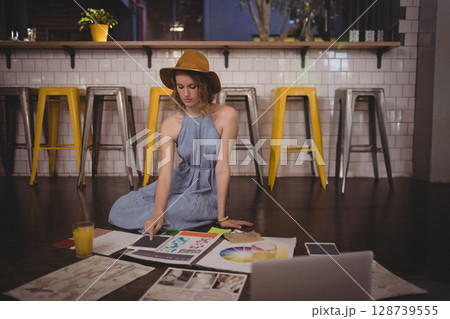 Reviewing female artist selecting sketches on wooden floor in studio, with tablet and orange juice 128739555