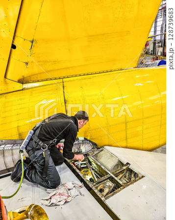 Aircraft technician performing inspection on yellow airplane stabilizer in hangar. High quality photo Aircraft technician performing inspection on yellow airplane stabilizer in hangar. High quality photo 128739683