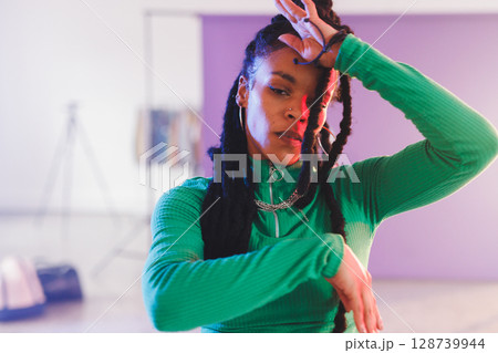 African American woman striking expressive dance pose in studio with tripod and purple backdrop 128739944
