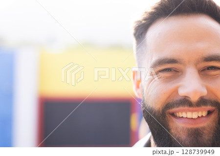 Young man smiling broadly in front of colorful painted mural outdoors, enjoying sunny mood 128739949
