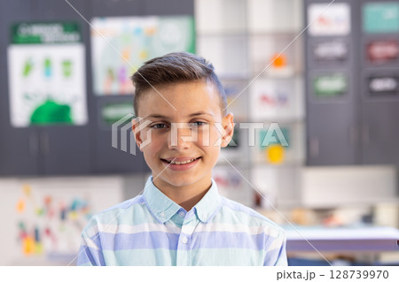 Teenage boy smiling at camera in art classroom, with colorful artwork and charts pinned on cabinets Teenage boy smiling at camera in art classroom, with colorful artwork and charts pinned on cabinets 128739970