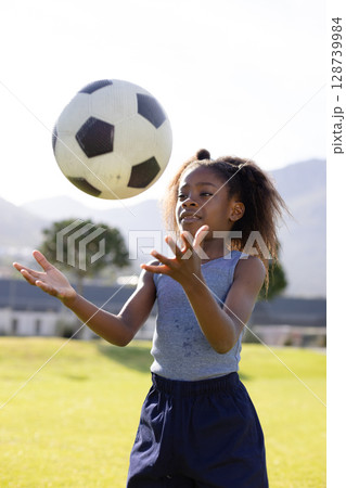 African American girl catching black-and-white soccer ball on grassy park field, showing skill African American girl catching black-and-white soccer ball on grassy park field, showing skill 128739984