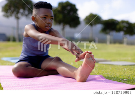 African American child boy stretching forward on pink mat in park, improving flexibility 128739995