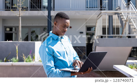 Middle aged African American man typing on laptop in outdoor courtyard, with concrete planter boxes Middle aged African American man typing on laptop in outdoor courtyard, with concrete planter boxes 128740071