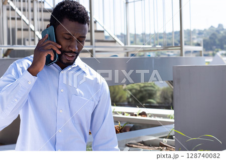 African American man talking on smartphone on urban balcony overlooking hillside, copy space 128740082