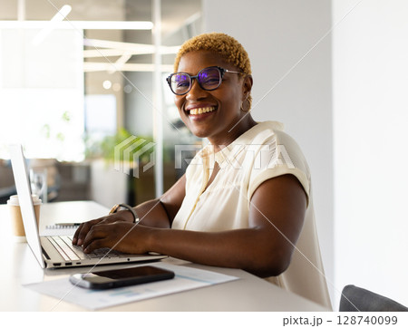 African American woman typing on laptop at desk in modern office with coffee cup, copy space African American woman typing on laptop at desk in modern office with coffee cup, copy space 128740099