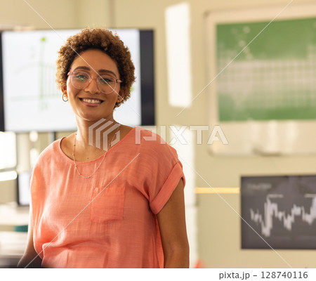 Woman standing in laboratory setting, with histogram and line graph monitors and green chart board 128740116