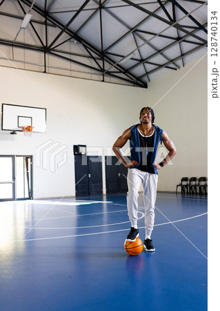 African American man standing with foot on basketball in indoor court, wearing whistle, copy space African American man standing with foot on basketball in indoor court, wearing whistle, copy space 128740134