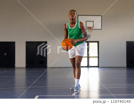 African American woman holding basketball, aiming shot on indoor basketball court with hoop, doors 128740140