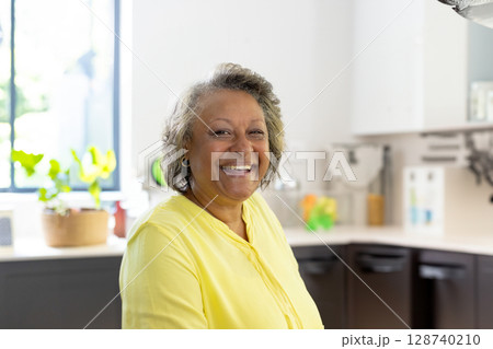 Senior woman smiling and organizing glass jars on gray countertop in home kitchen with potted plant 128740210