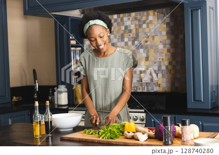 African American woman chopping lettuce and mushrooms on cutting board at kitchen island 128740280